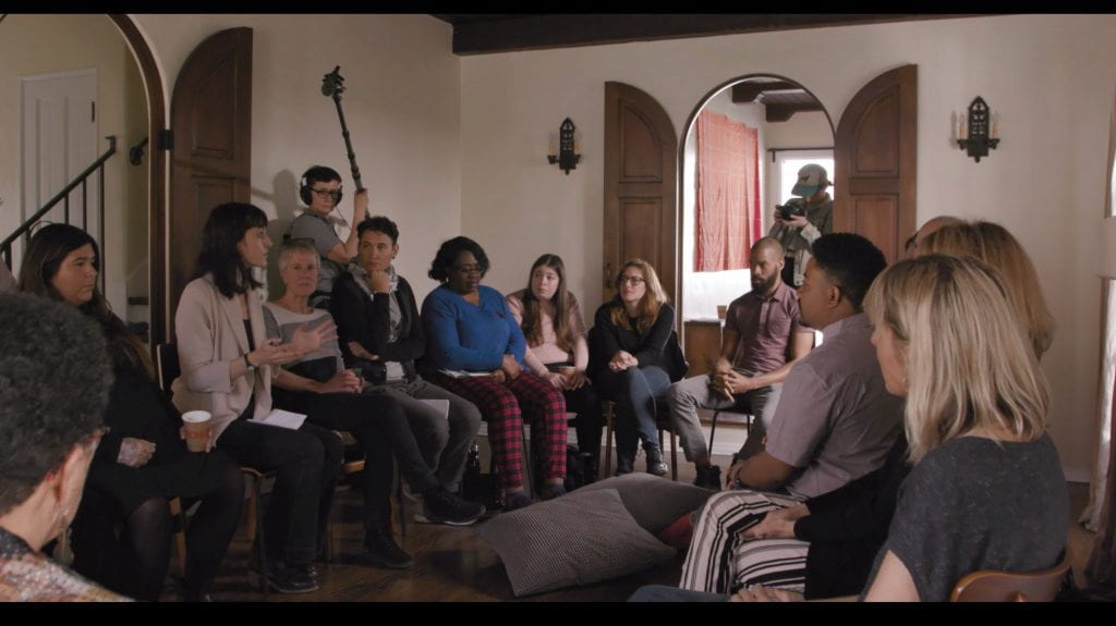 People sitting in a circle in a room with a camera and sound crew around them